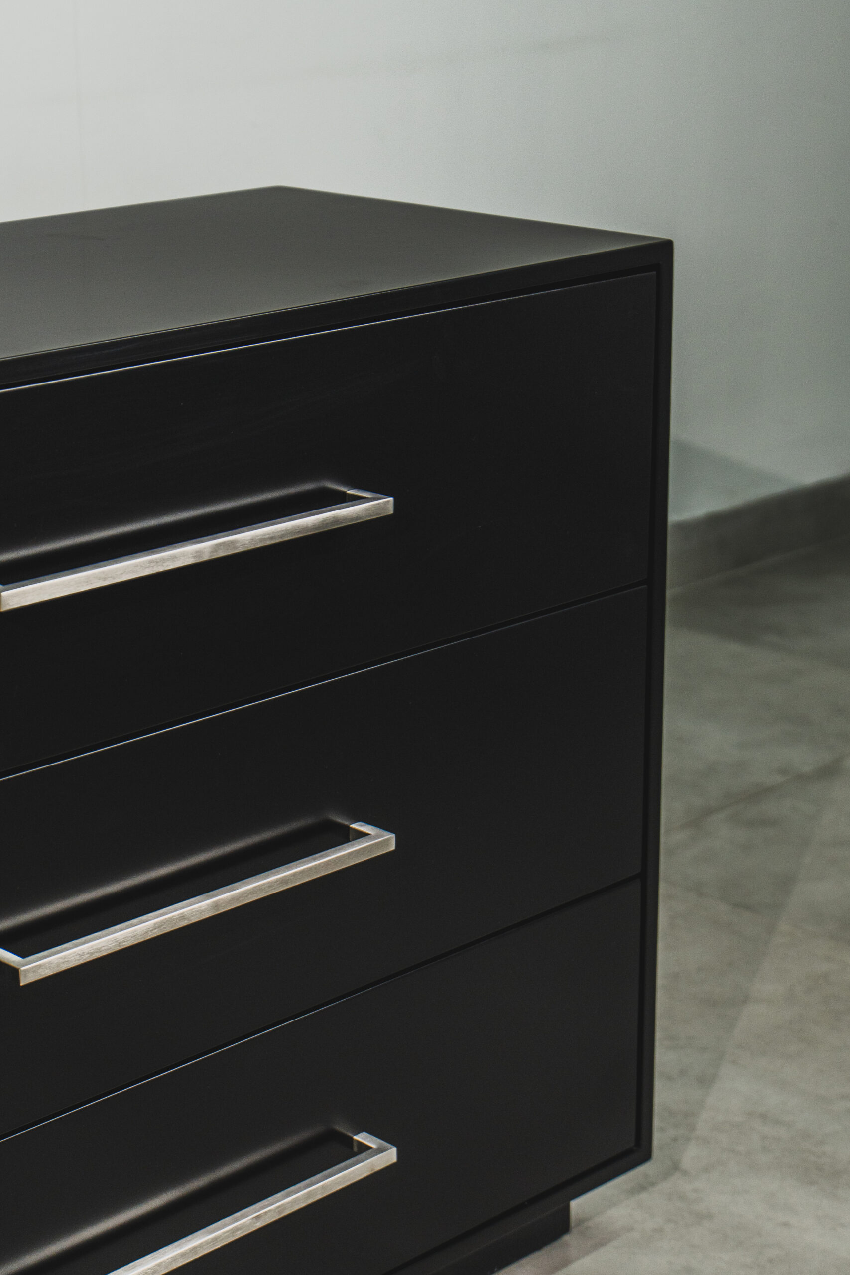 Close-up of modern black chest of drawers with sleek silver handles, contemporary bedroom storage furniture detail.