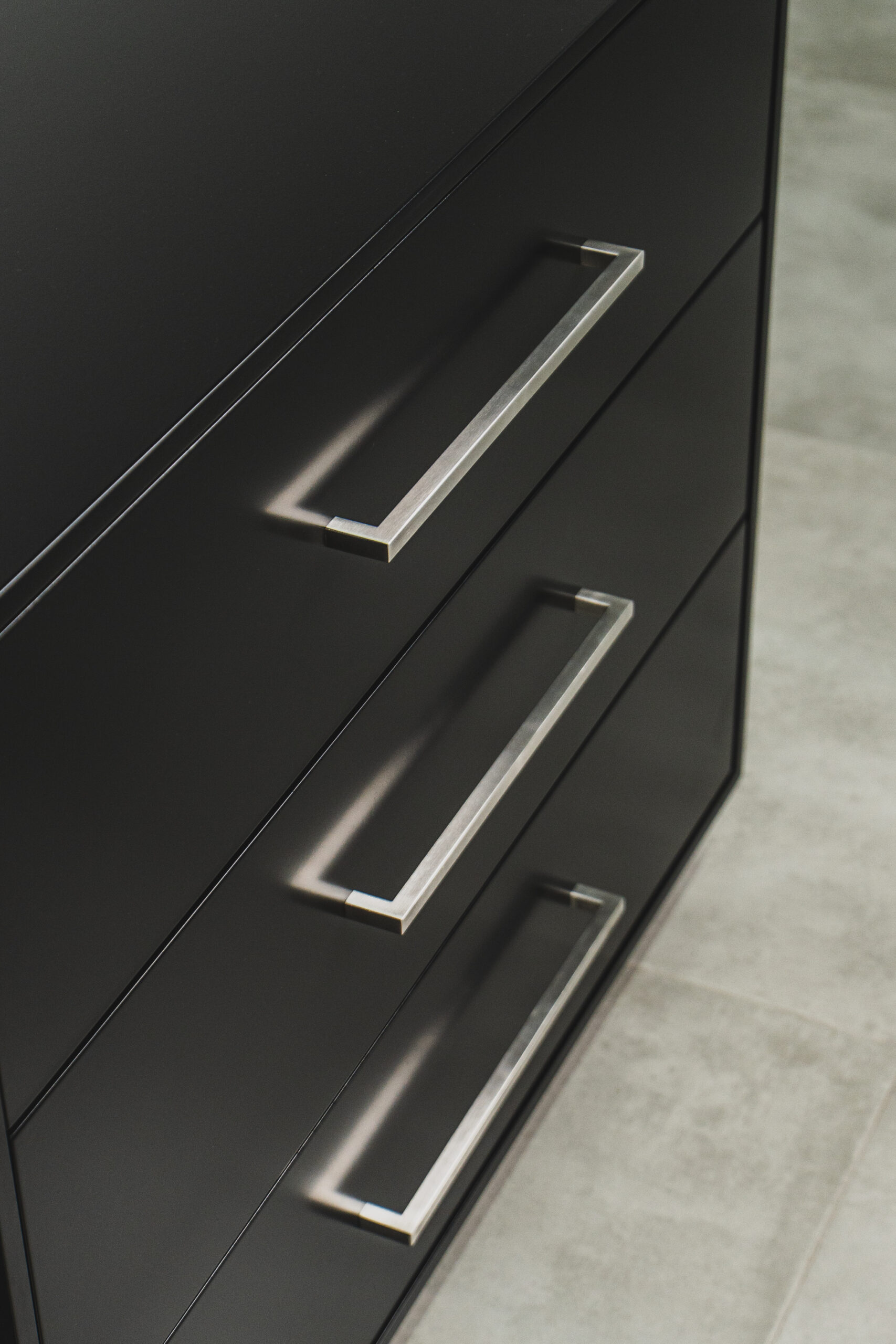 Close-up of black chest of drawers with modern silver handles, sleek bedroom storage furniture detail.