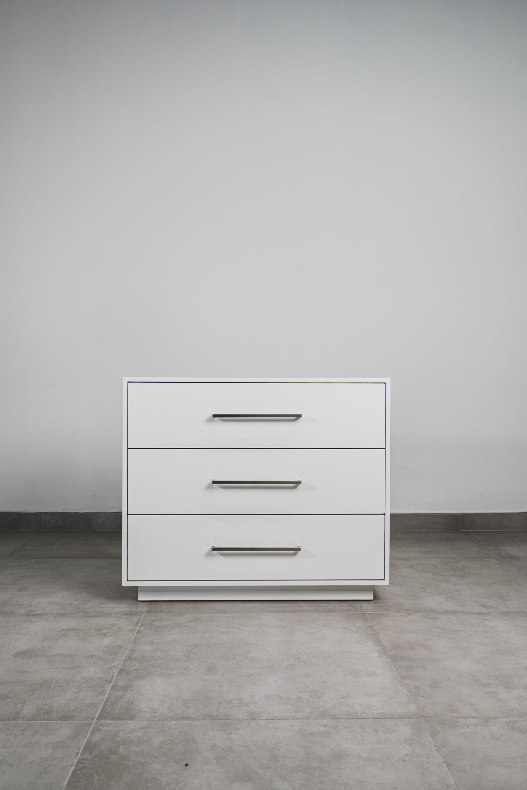 White 3-drawer bedside pedestal with sleek metal handles, displayed on a tiled floor.