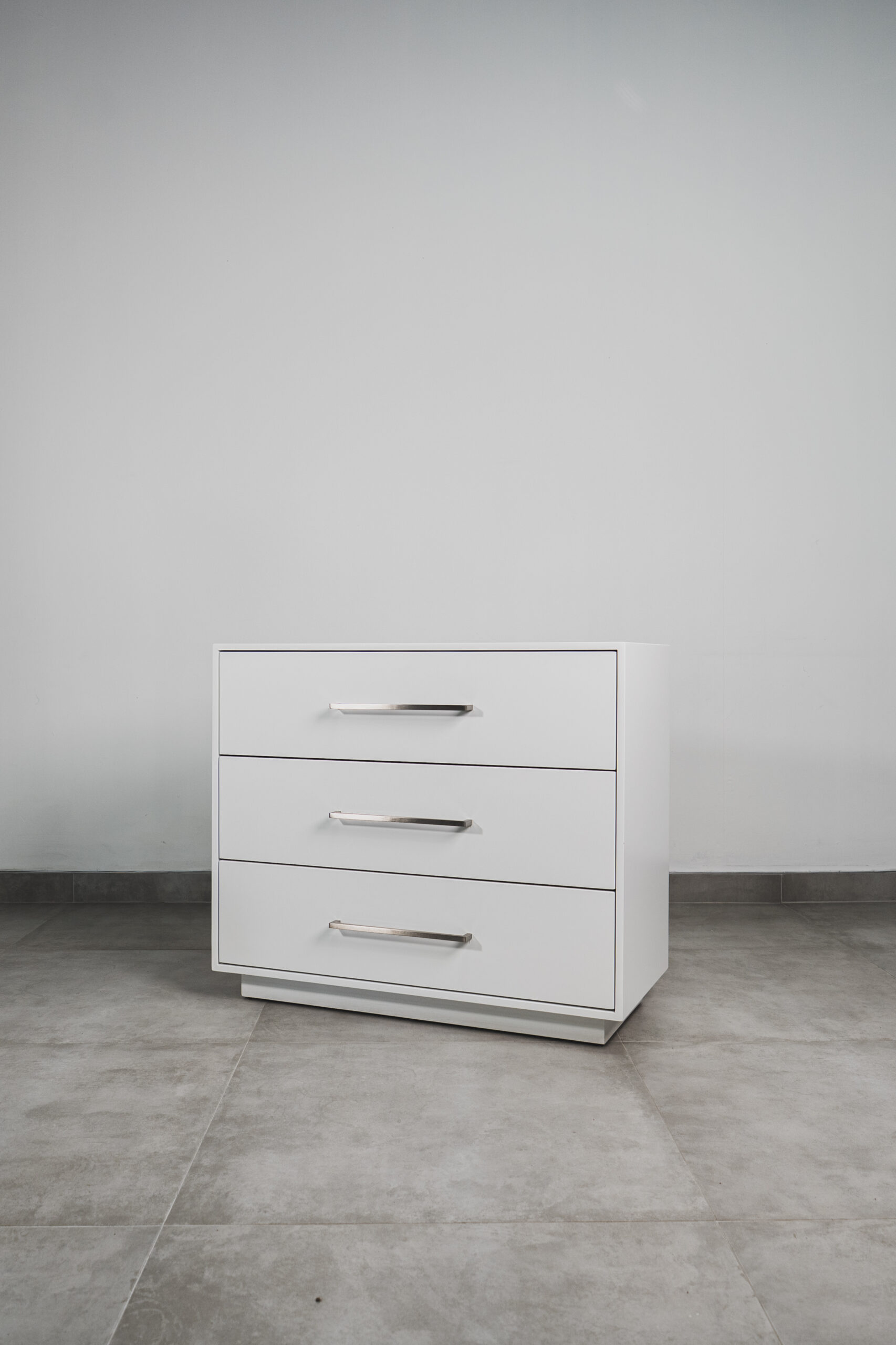 Modern white 3-drawer chest with metal handles on a tiled floor