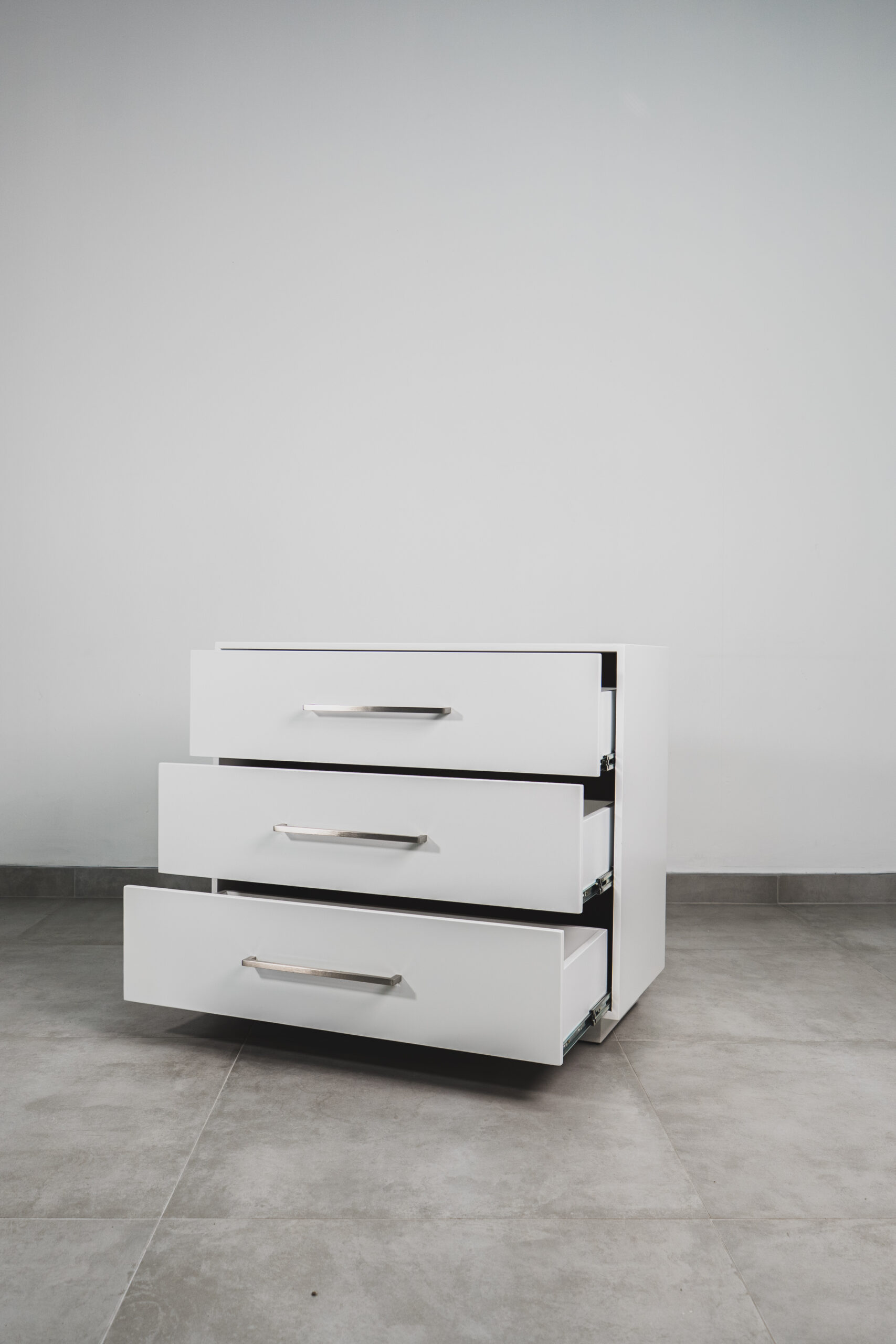 White 3-drawer bedside pedestal with metal handles and all drawers open, shown on a tiled floor.