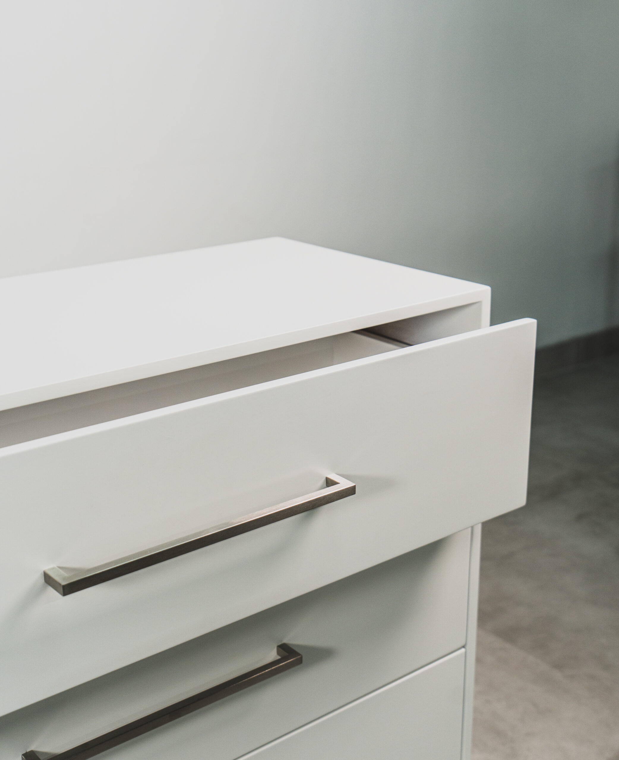 Close-up of a white 3-drawer pedestal with an open top drawer and modern metal handles.