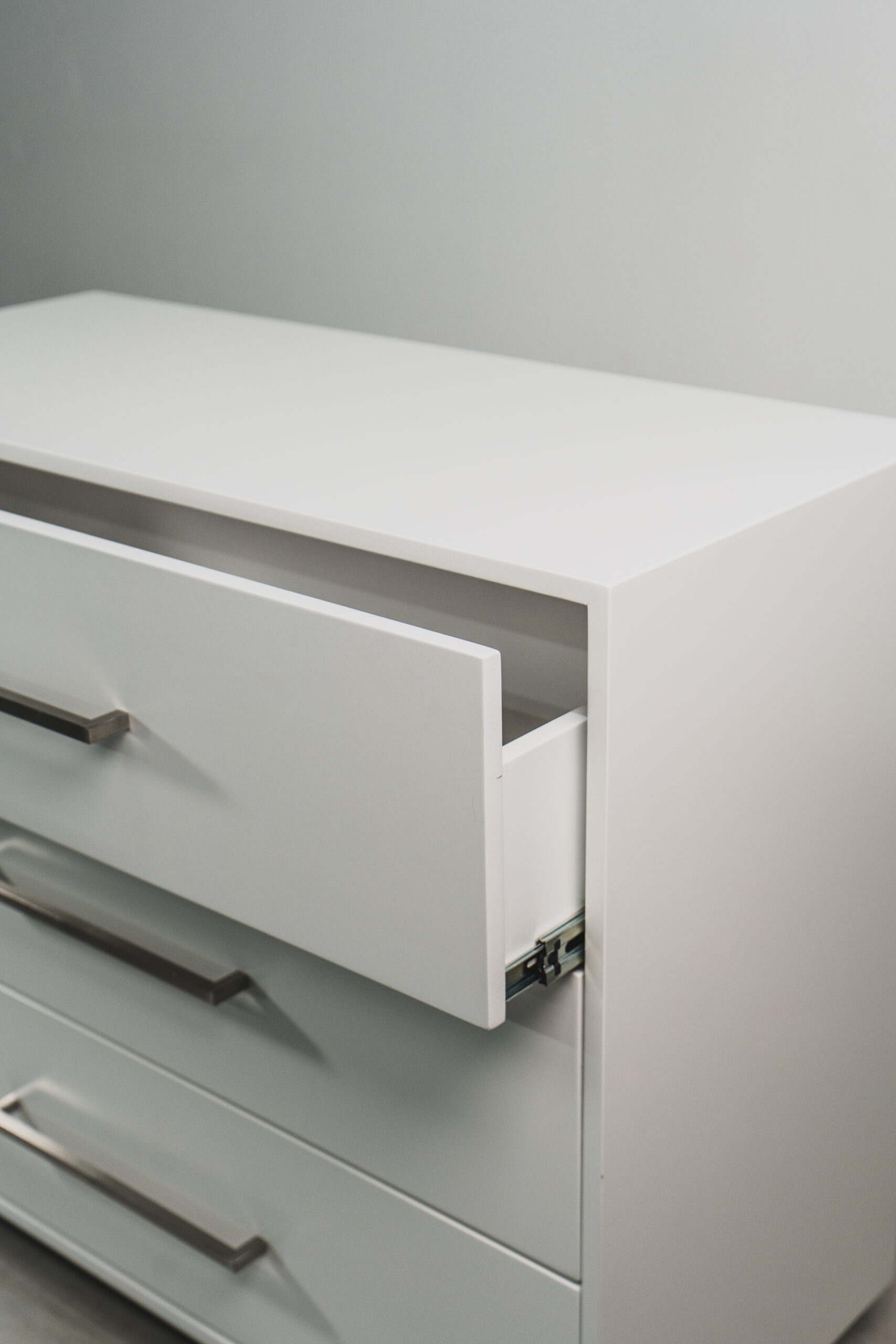 Side view of a white 3-drawer pedestal with an open drawer and modern metal handles.