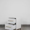 White bedside table with two drawers open, featuring gold handles and a gold steel base, displayed on a grey tiled floor.