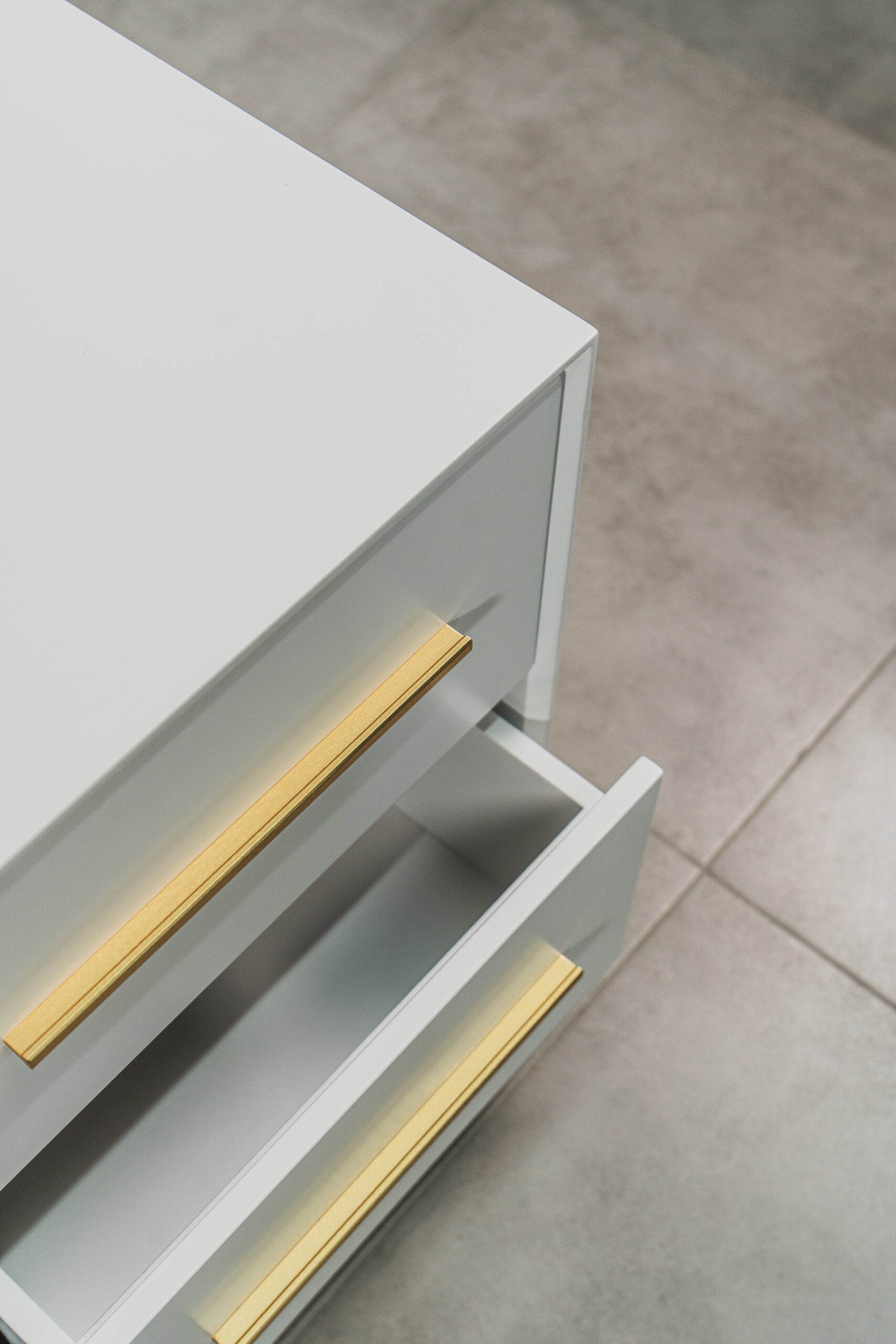 Top view of a white bedside table with two drawers slightly open, featuring sleek gold handles and a modern minimalist design.