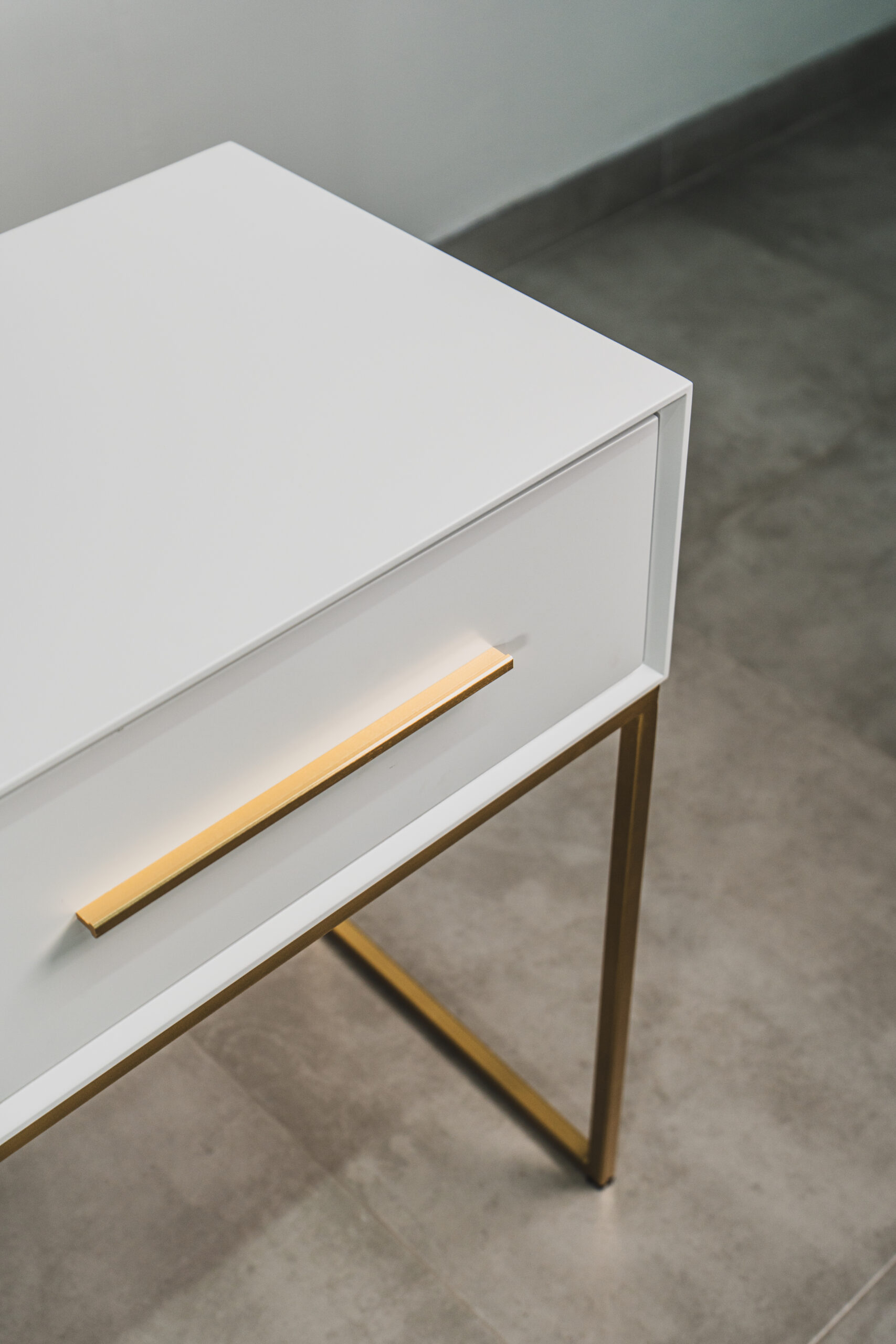 Close-up of white dressing table with gold handle and slim gold metal legs, showcasing modern minimalist bedroom furniture design.