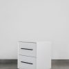 Modern white two-tone side table with black handles and black steel base, featuring two drawers and a minimalist design.