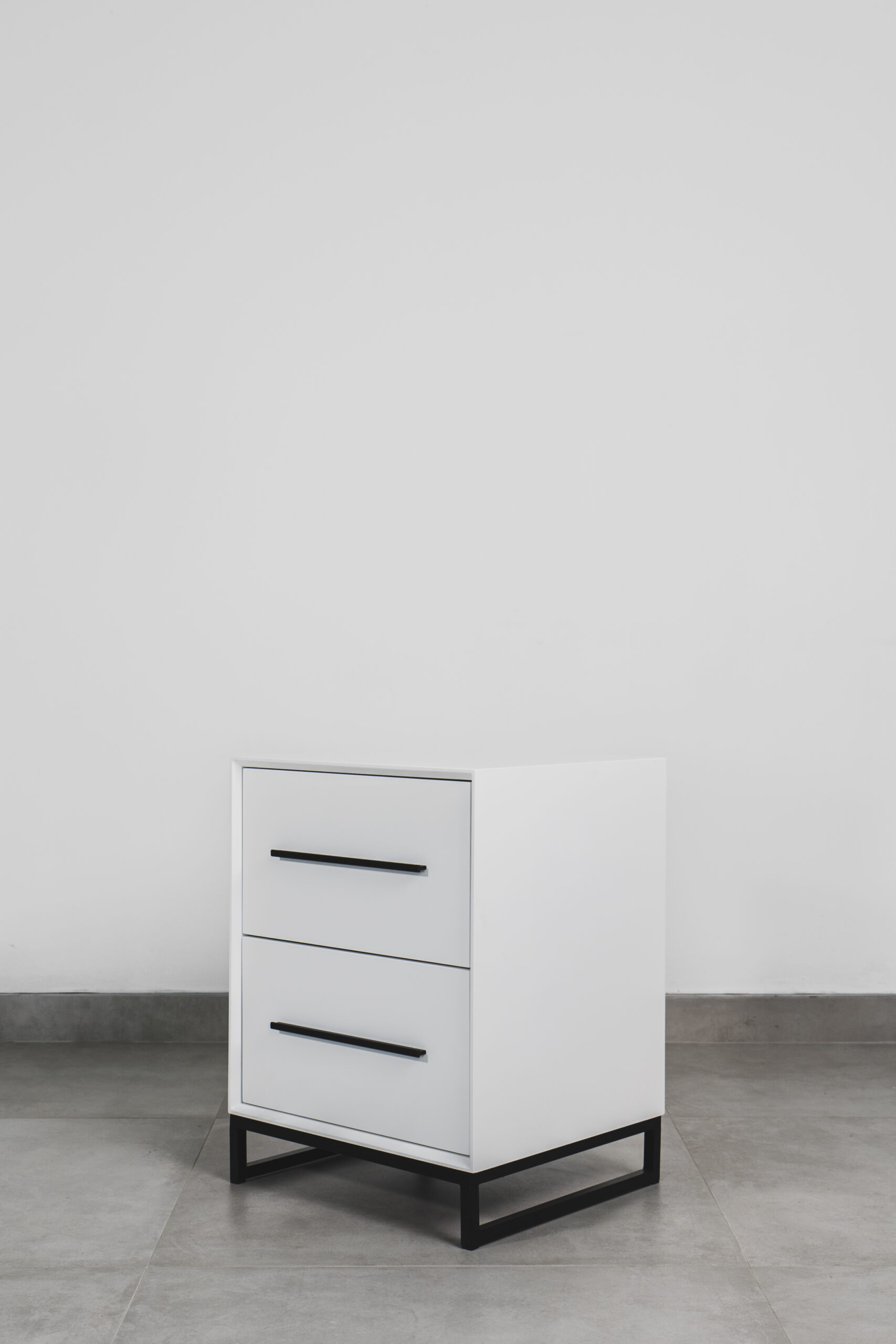 Modern white two-tone side table with black handles and black steel base, featuring two drawers and a minimalist design.