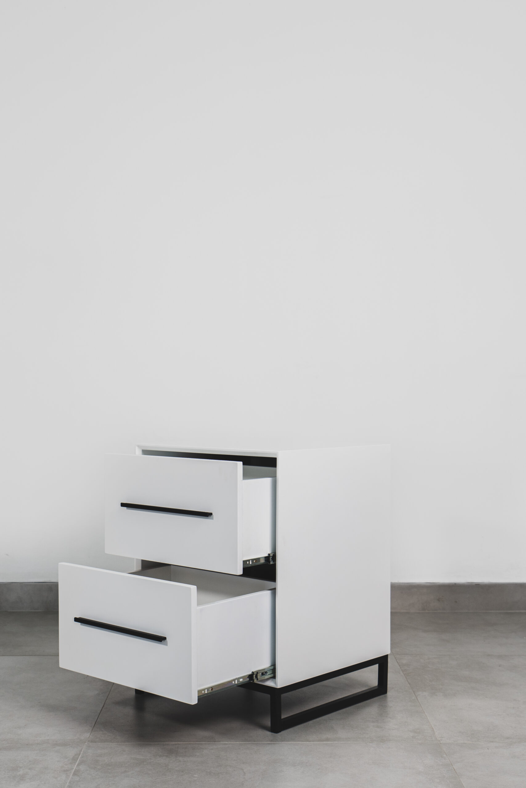 Modern white two-tone side table with black handles and steel base, featuring two open drawers and a sleek minimalist design.