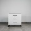 Monochrome white 3 drawer chest of drawers with black handles and steel base on a tiled floor.