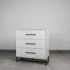 Modern white 3-drawer chest of drawers with black handles and steel base on tiled floor.