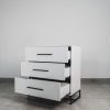 Monochrome white 3 drawer chest of drawers with black handles and a black steel base, shown with drawers open on a tiled floor.