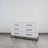 White six-drawer chest of drawers with black handles and steel base on tiled floor, ideal for modern bedroom storage.