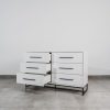 White six-drawer chest of drawers with black handles and open drawers on steel base, showcasing modern minimalist storage design.
