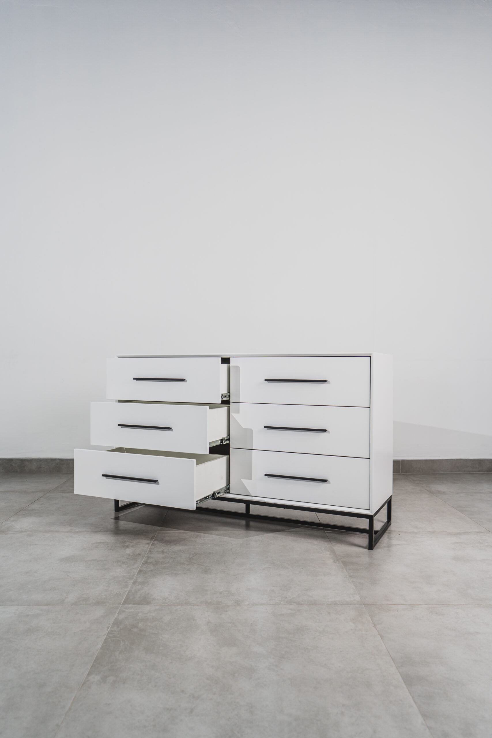 White six-drawer chest of drawers with black handles and open drawers on steel base, showcasing modern minimalist storage design.