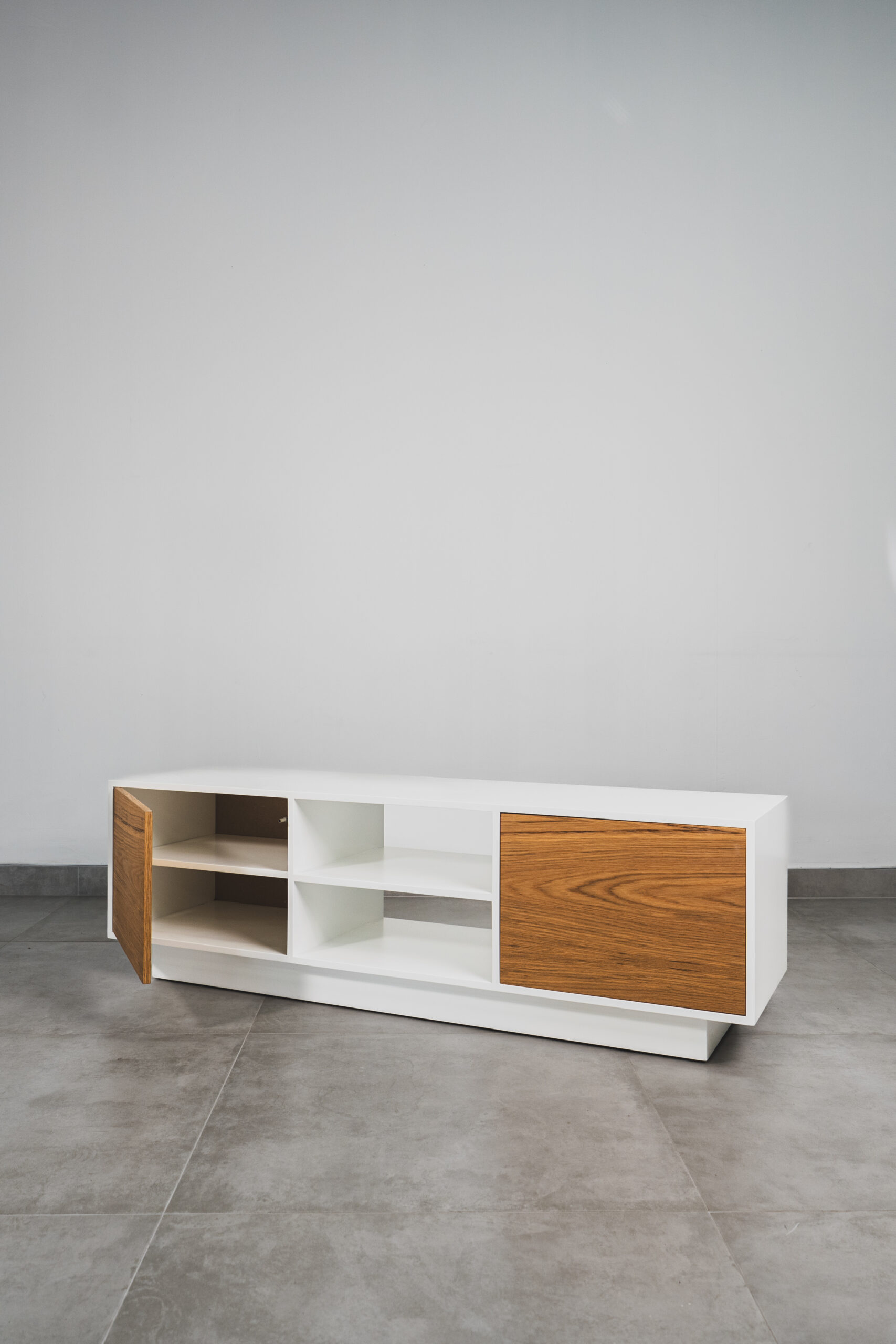 Modern Scandinavian white TV unit with natural wood doors, open centre shelves, and one cupboard door open, showcasing minimalist design and functional storage.