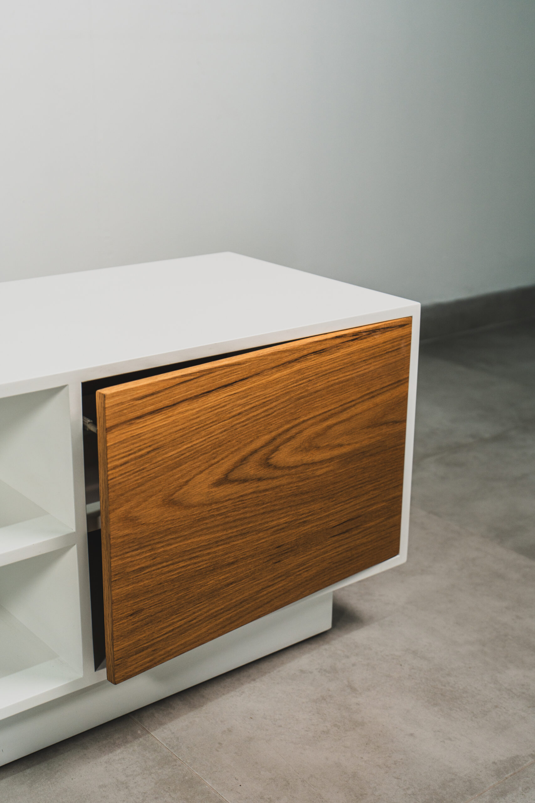 Close-up of Scandinavian white TV cabinet with natural wood door slightly open, featuring clean lines and minimalist modern design.
