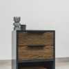Modern wood side table with a dark grey frame, featuring two wood veneer drawers and an open shelf at the base holding an orange book, styled with minimalist glass decor on top.