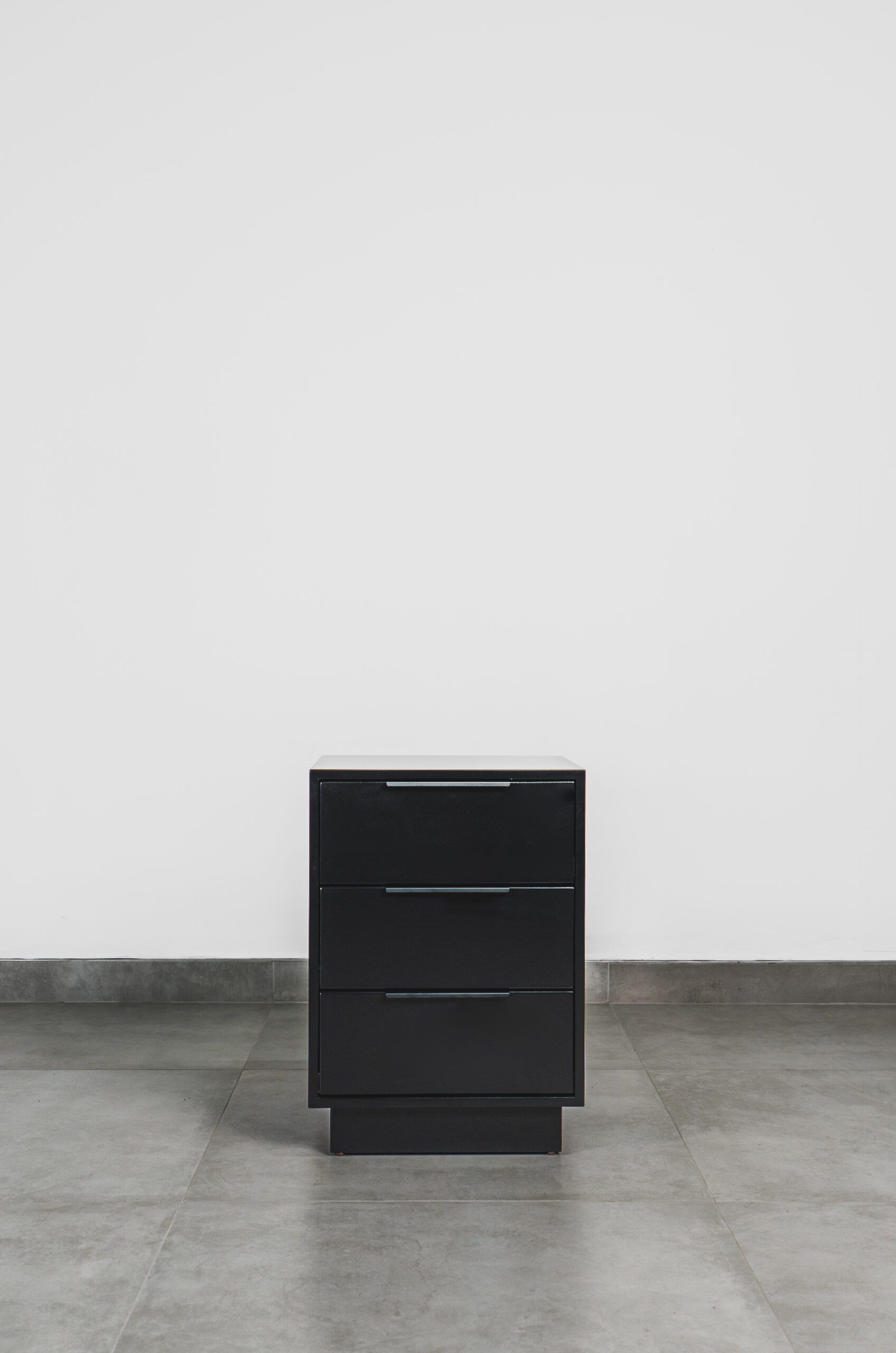 Front view of a modern black side table with three drawers, featuring a clean matte finish and minimalist pedestal base.