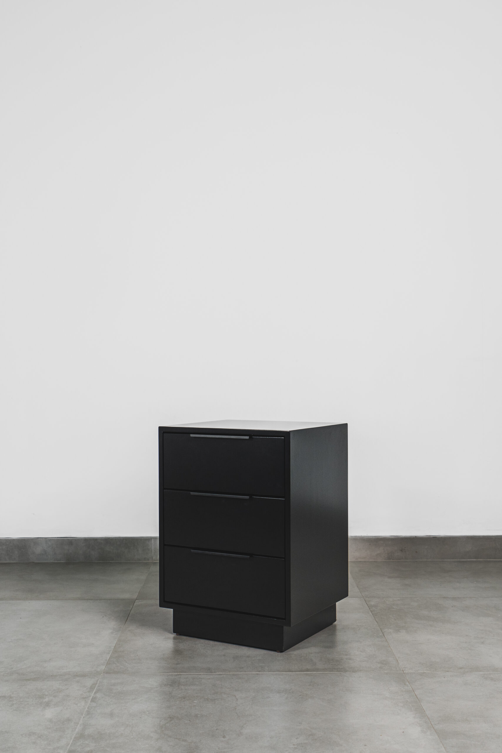 Modern black side table with three drawers and a sleek matte finish, ideal as a contemporary bedside pedestal.