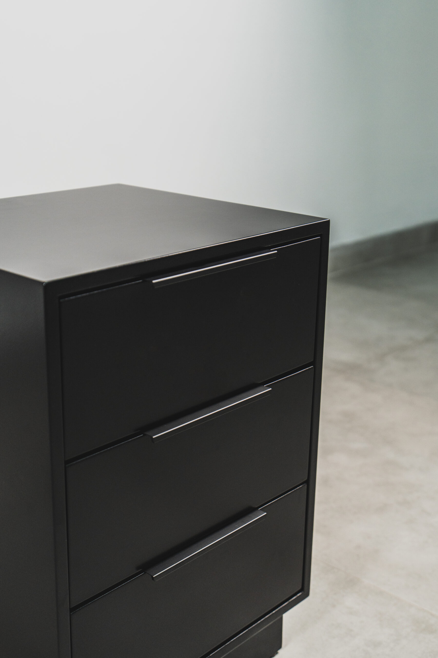 Close-up of a sleek black bedside table with three drawers, showcasing a smooth matte finish and minimalist handles.