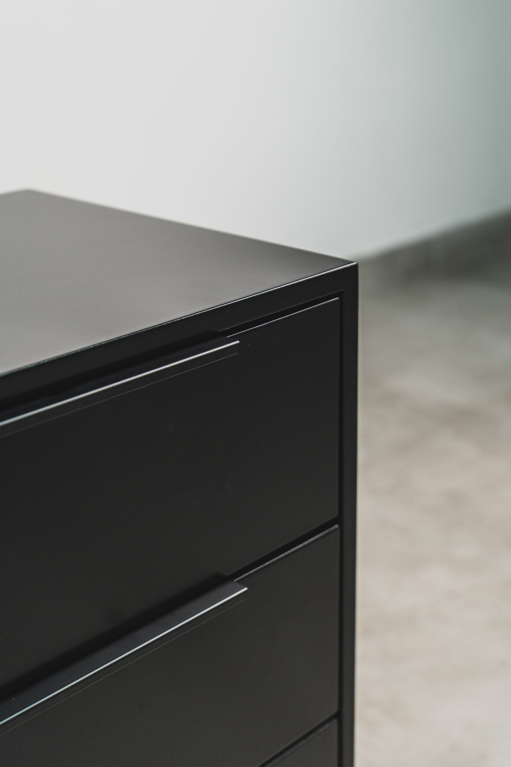 Detail view of a modern black three-drawer bedside table with sleek handles and a smooth matte finish.