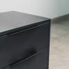 Close-up of a sleek dark grey pedestal with three drawers and minimalist black handles.