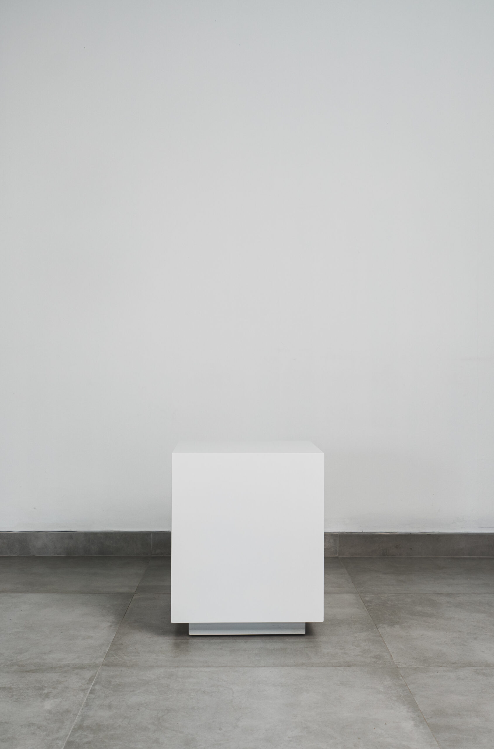 Modern white cube side table with a sleek minimalist design, set against a neutral wall and tiled floor.