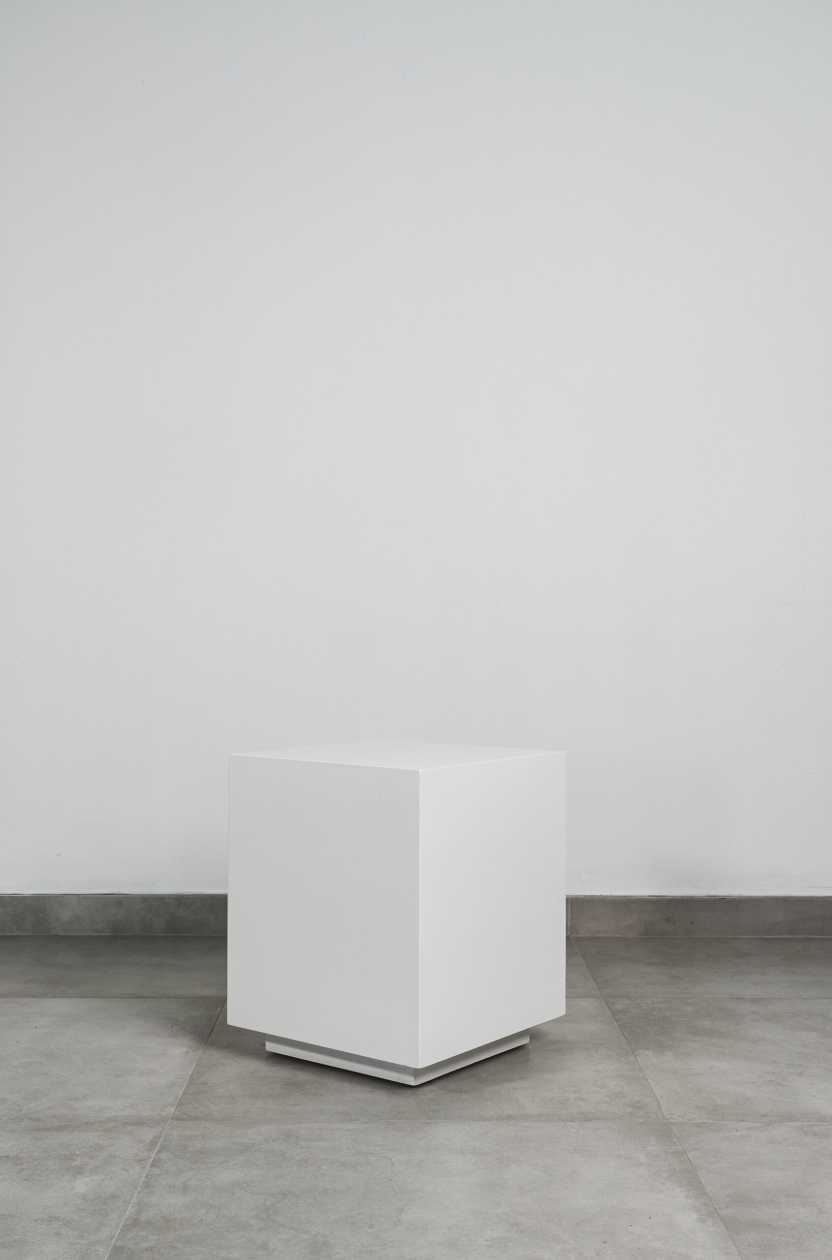 Modern white cube side table with a minimalist design, shown on a grey tiled floor against a light wall.