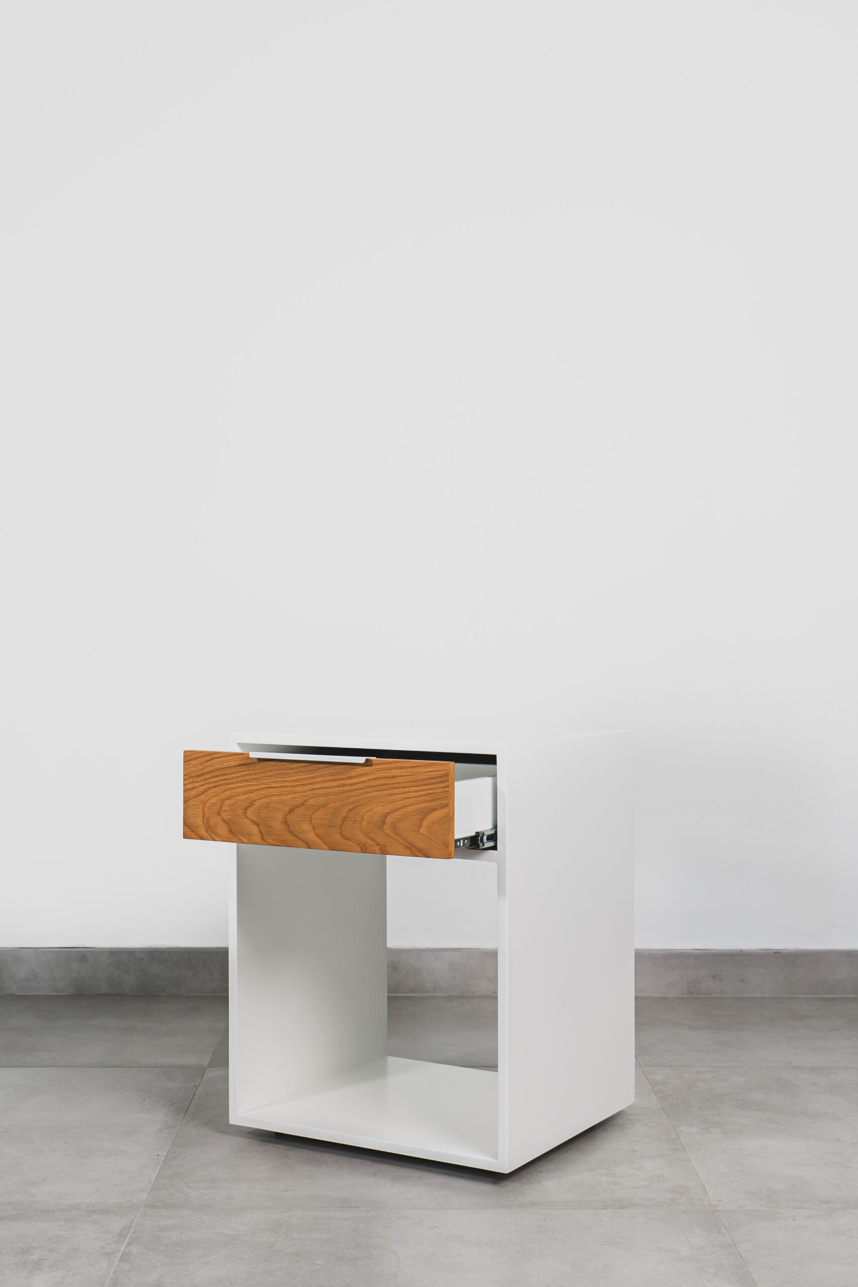 White pedestal with a wooden drawer partially open, featuring a minimalist modern design and open lower shelf on a tiled floor.