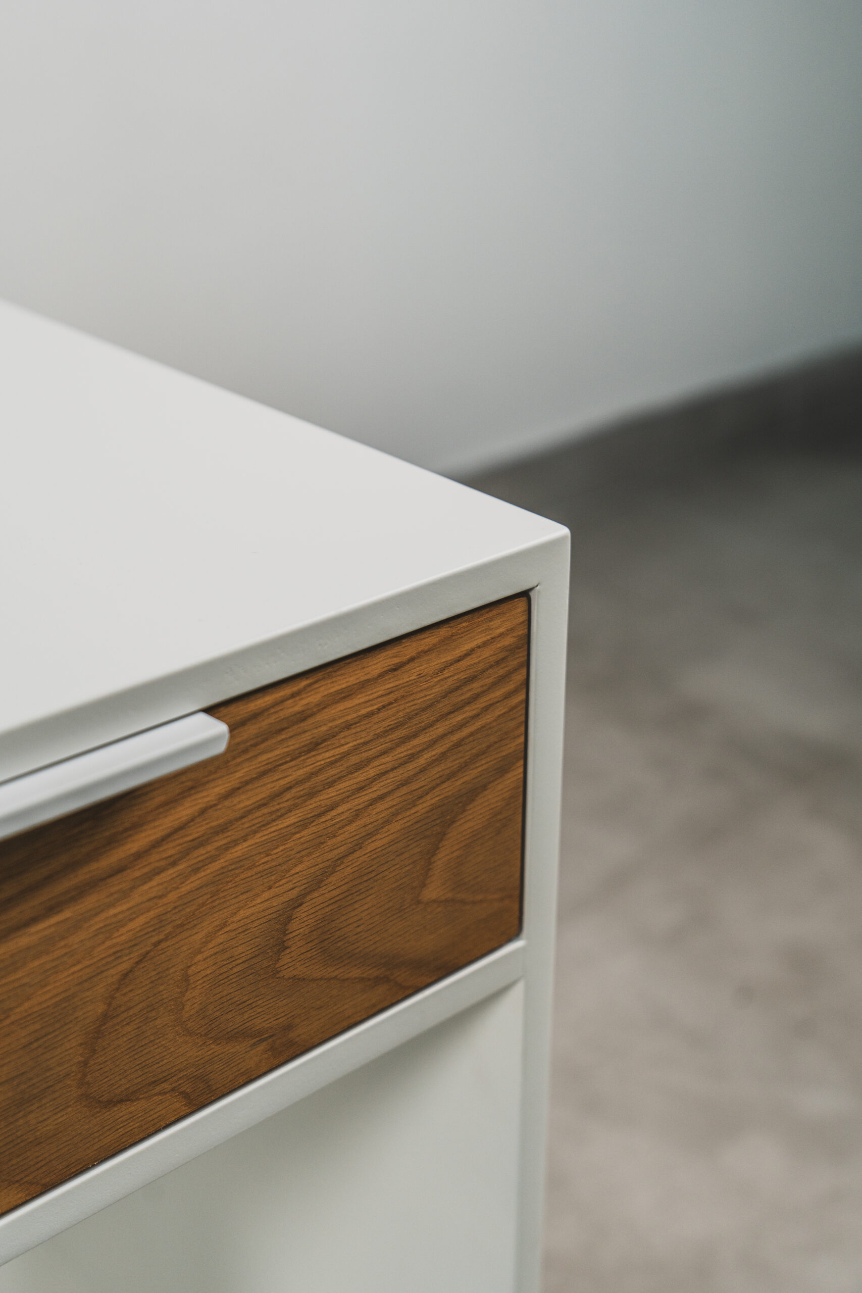 Close-up of a white pedestal corner showing a wooden drawer front and sleek handle, highlighting the smooth finish and modern design.