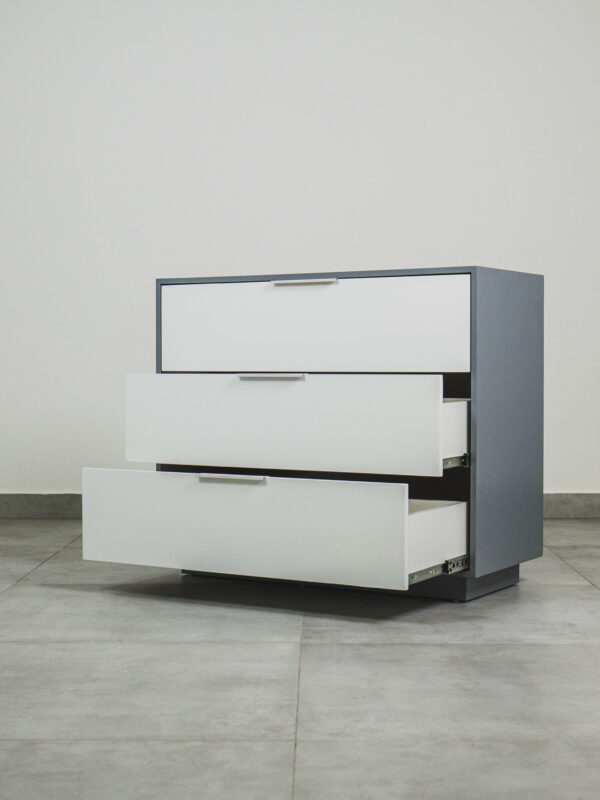 Grey and white compactum chest of drawers with three drawers partially open, showing smooth metal runners and a modern minimalist design