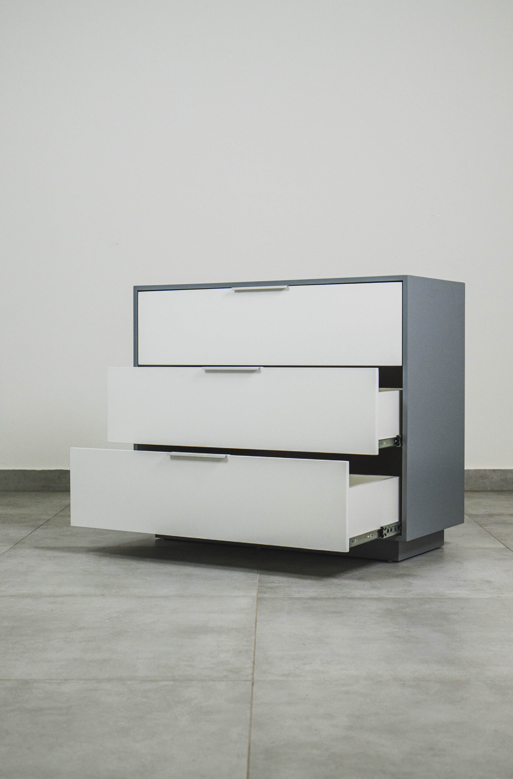 Grey and white compactum chest of drawers with three drawers partially open, showing smooth metal runners and a modern minimalist design