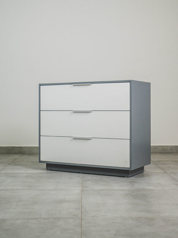 Modern grey and white compactum chest of drawers with three white-front drawers and silver handles, shown angled
