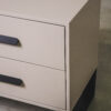 Close-up of a greige two-drawer pedestal showing smooth drawer fronts and black metal handles.